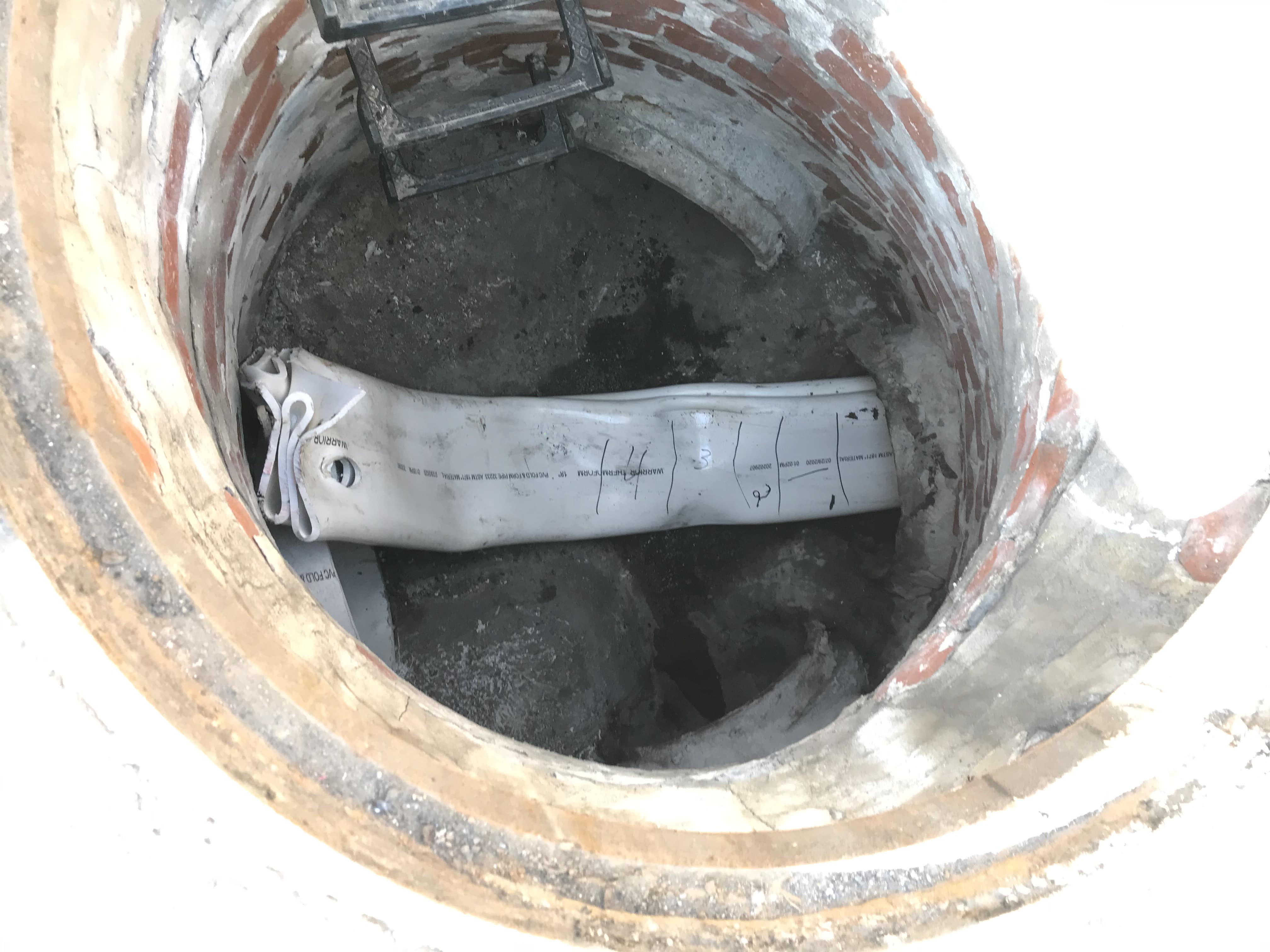 An image of the inside of a manhole cover where the special white PVC liner has been successfully pulled through the pipe